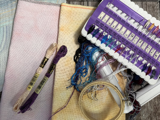 Embroidery tools including thread, hoop, and a purple embroidery kit on a wooden surface.