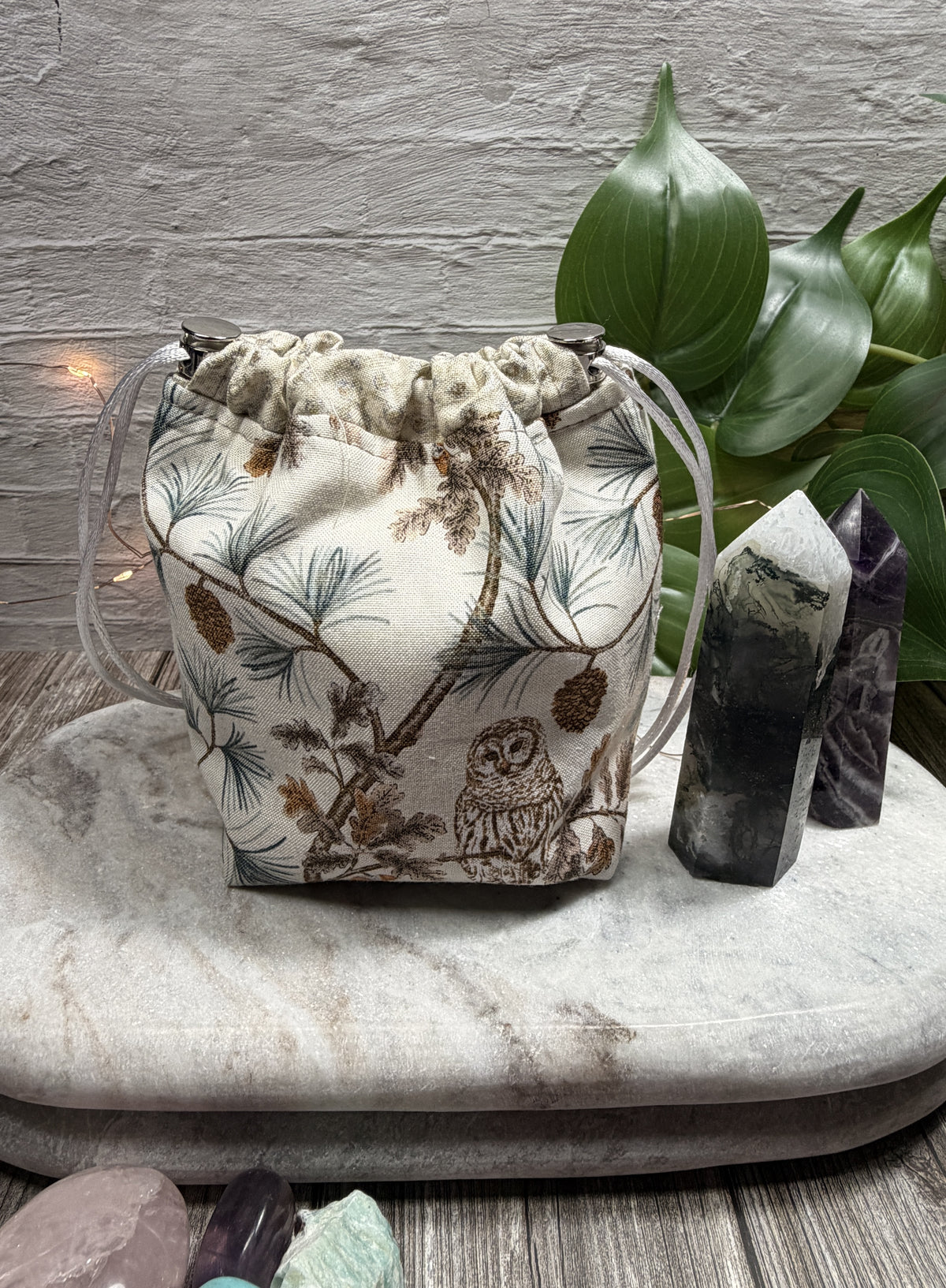 Drawstring bag with nature-themed design on a marble surface with crystals and plants.