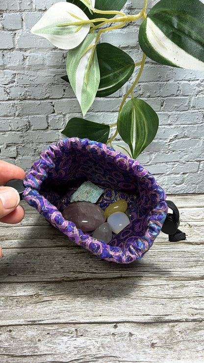 Purple drawstring pouch with crystal and stones on a wooden surface