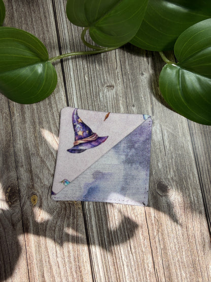 Square fabric page marker / bookmark  with a purple flower design on a wooden surface with green leaves.
