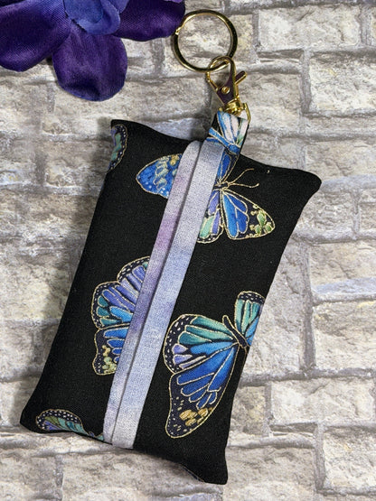 Fabric tissue pouch with a blue colourful butterfly pattern on a keychain against a stone wall background