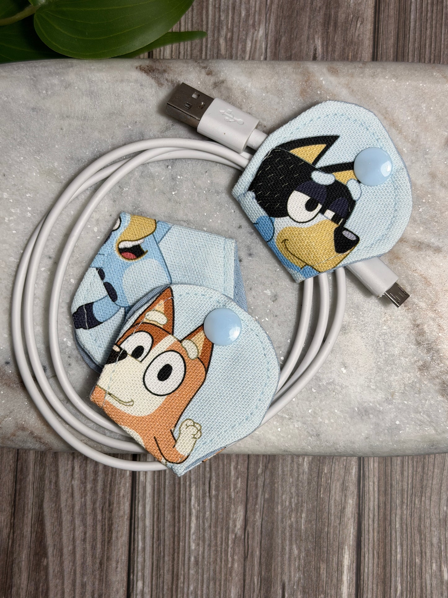 Bluey cable organiser with a mobile phone charger on a marble surface 