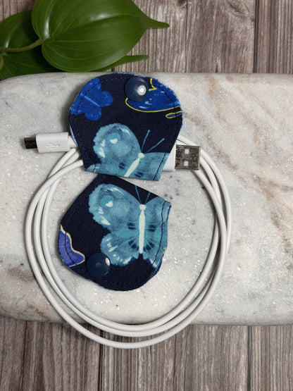Blue butterfly-shaped cable organiser with a mobile phone charger on a marble surface 