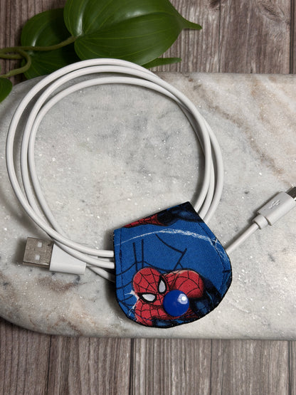 Spider-Man themed cable clip on a coiled USB cable with a plant in the background