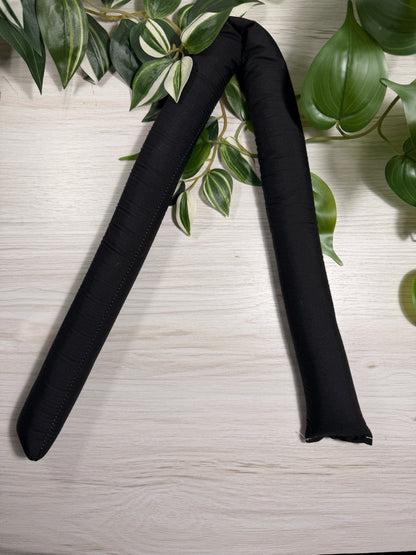 Black fabric and sand draught stopper on a wooden surface with leaves.