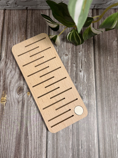 Wooden floss bobbin organiser on a wooden surface with a plant in the corner