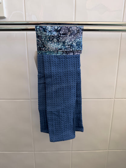 Blue textured towel hanging on a towel rack against a tiled bathroom wall.