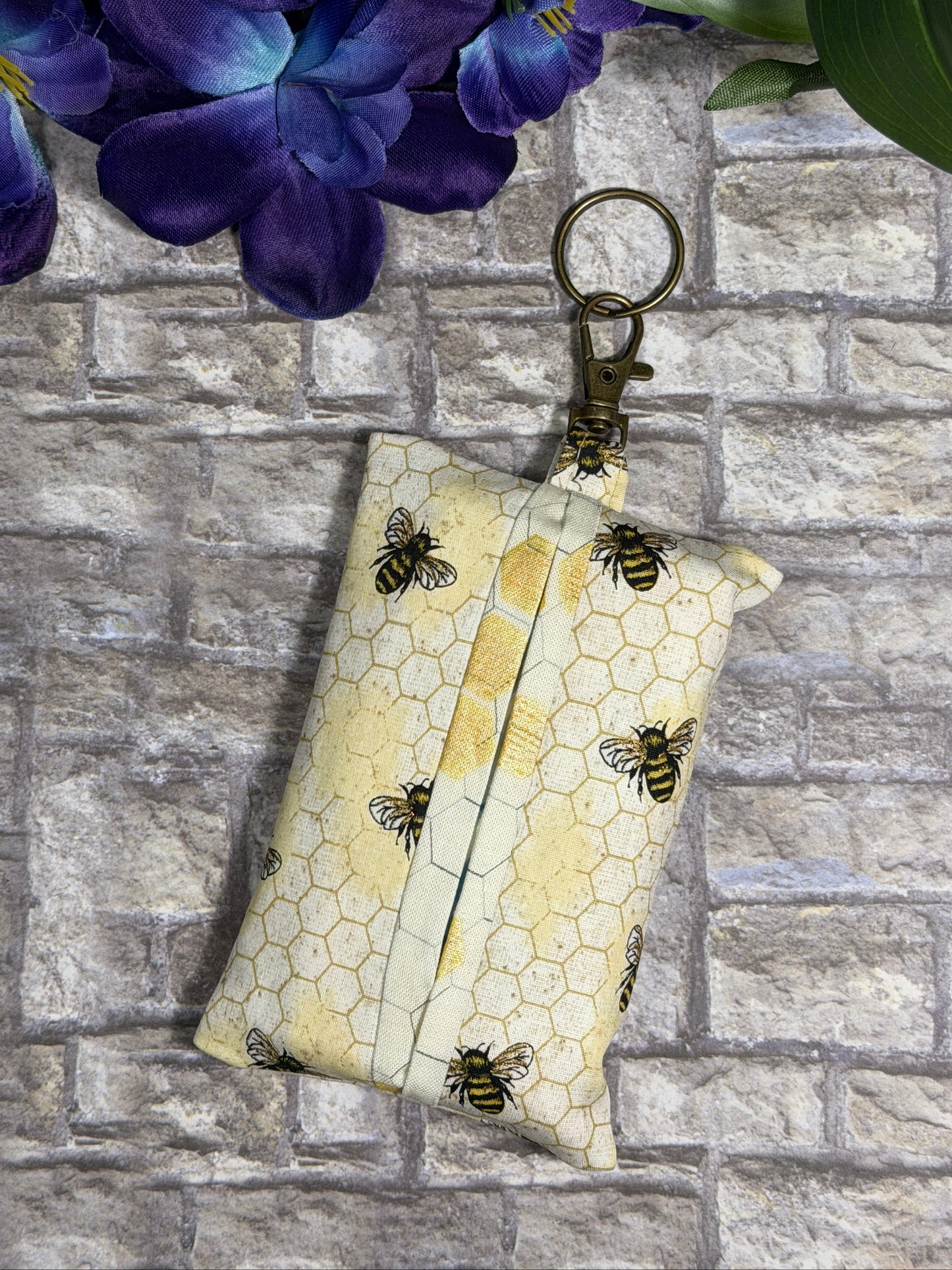 Fabric tissue pouch with a bees and honeycomb pattern on a keychain against a stone wall background