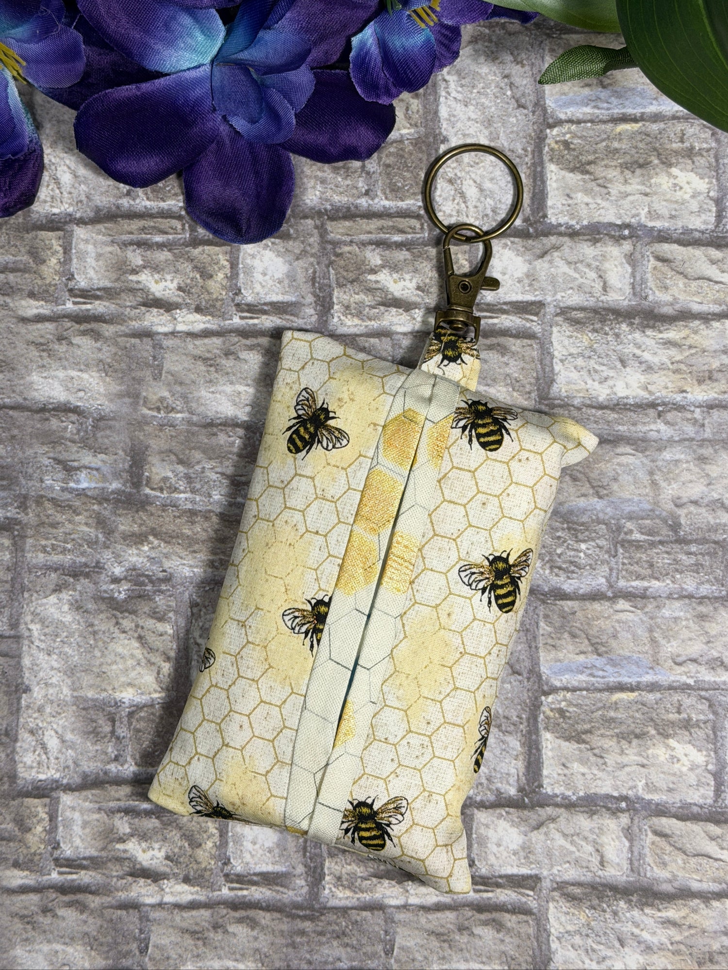 Fabric tissue pouch with a bees and honeycomb pattern on a keychain against a stone wall background