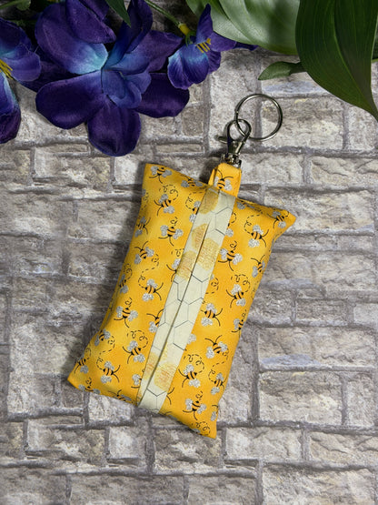 Fabric tissue pouch with a bees and honeycomb pattern on a keychain against a stone wall background