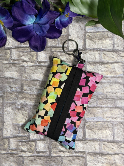 Fabric tissue pouch with a colourful pattern on a keychain against a stone wall background
