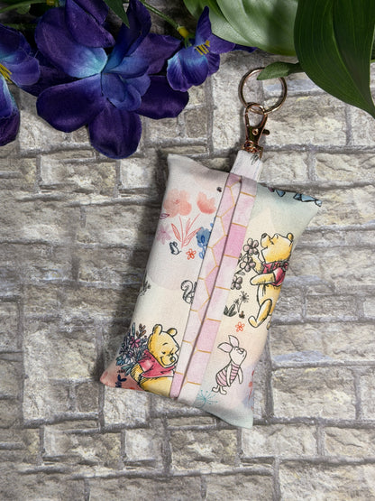 Fabric tissue pouch with a whinnie the Pooh pattern on a keychain against a stone wall background