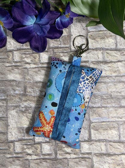 Fabric tissue pouch with a sea side pattern on a keychain against a stone wall background