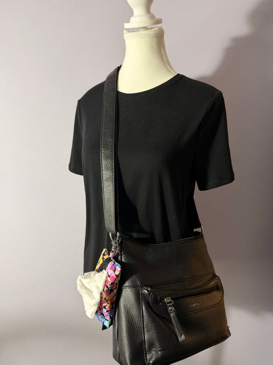 Black leather handbag with colorful tissue pouch with a white background