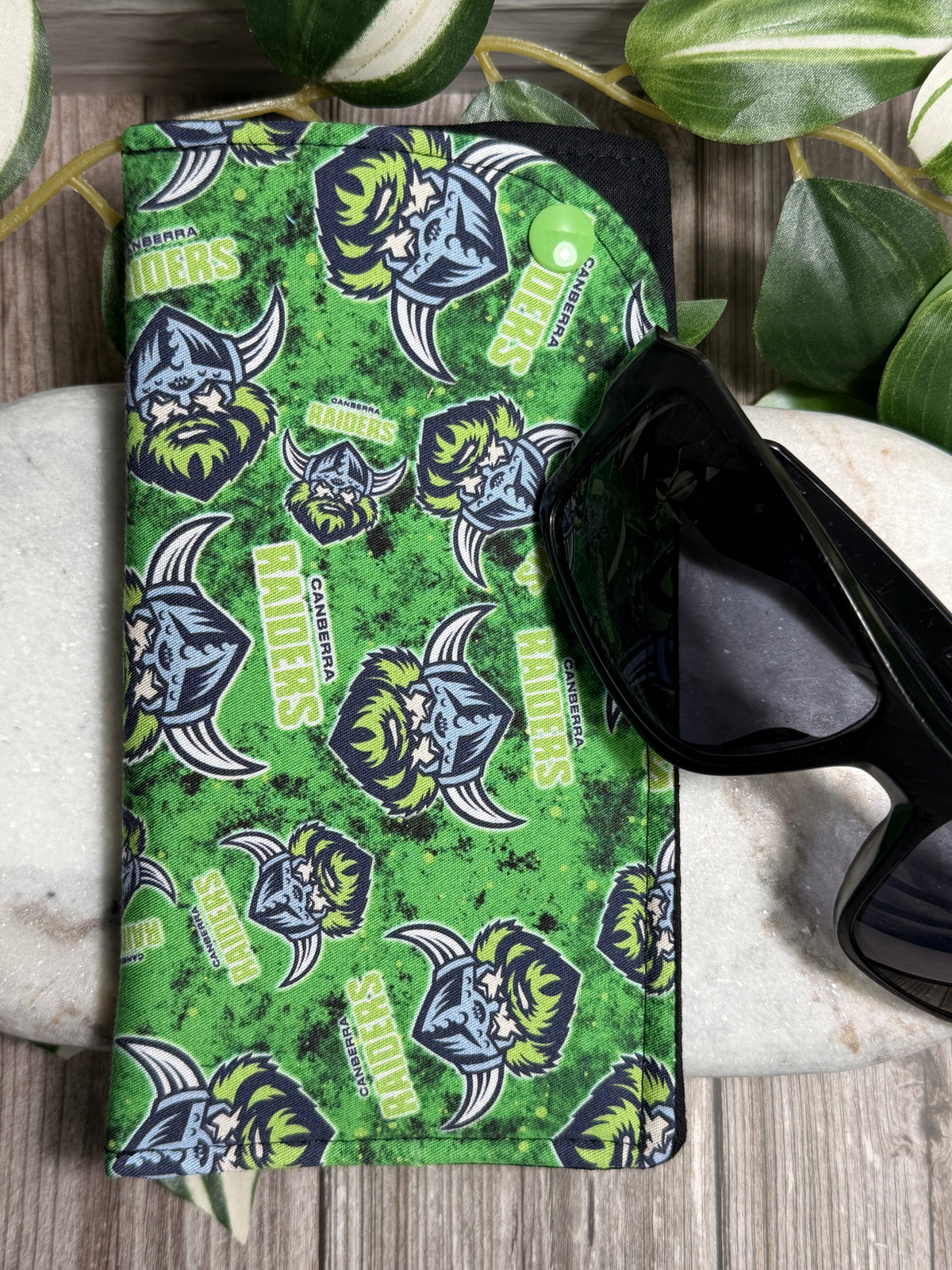 Glasses case with a Green patterned logo pattern and sunglasses on a wooden surface