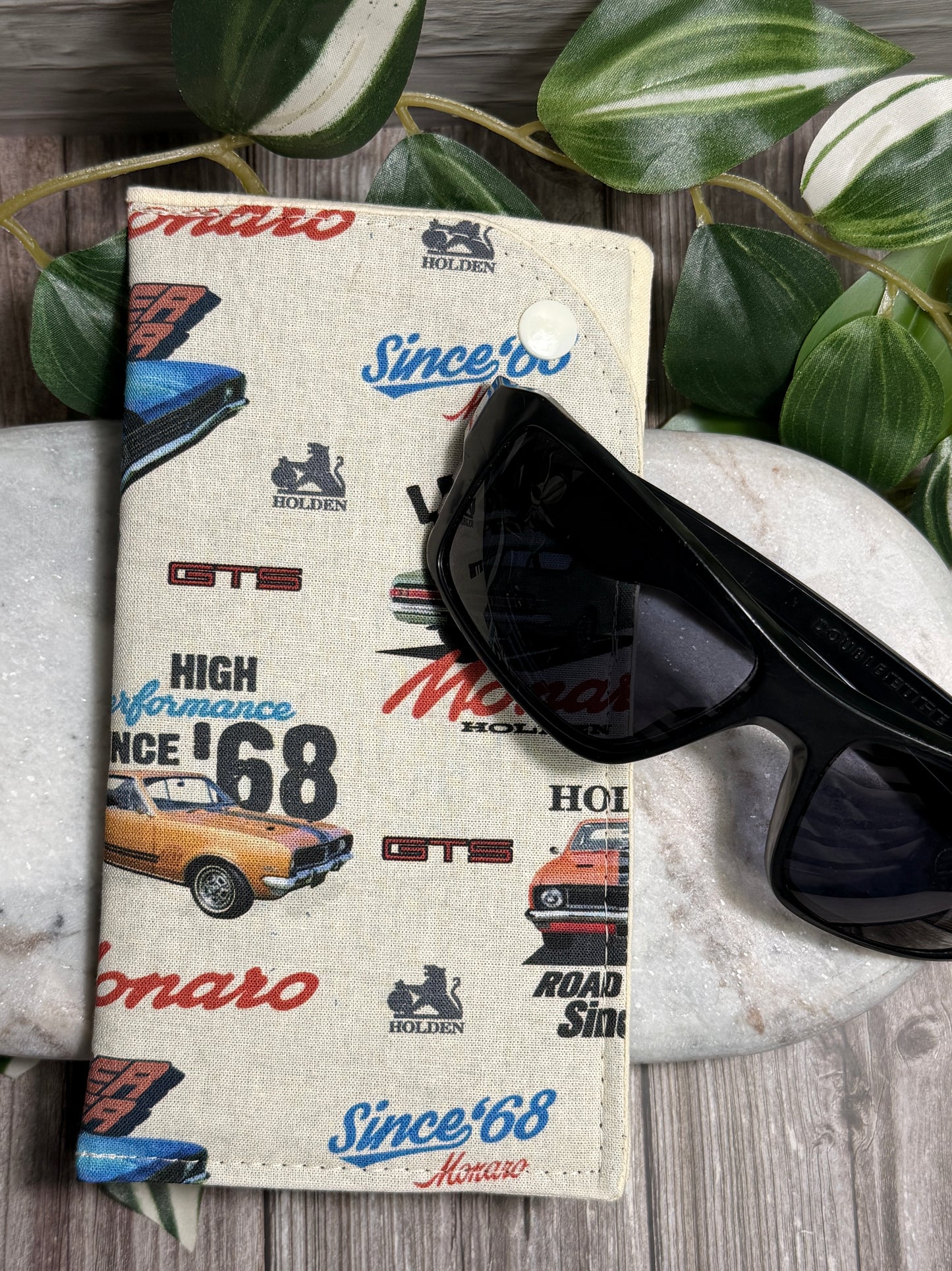 Glasses Case with vintage car brand designs and sunglasses on a stone surface with leaves in the background