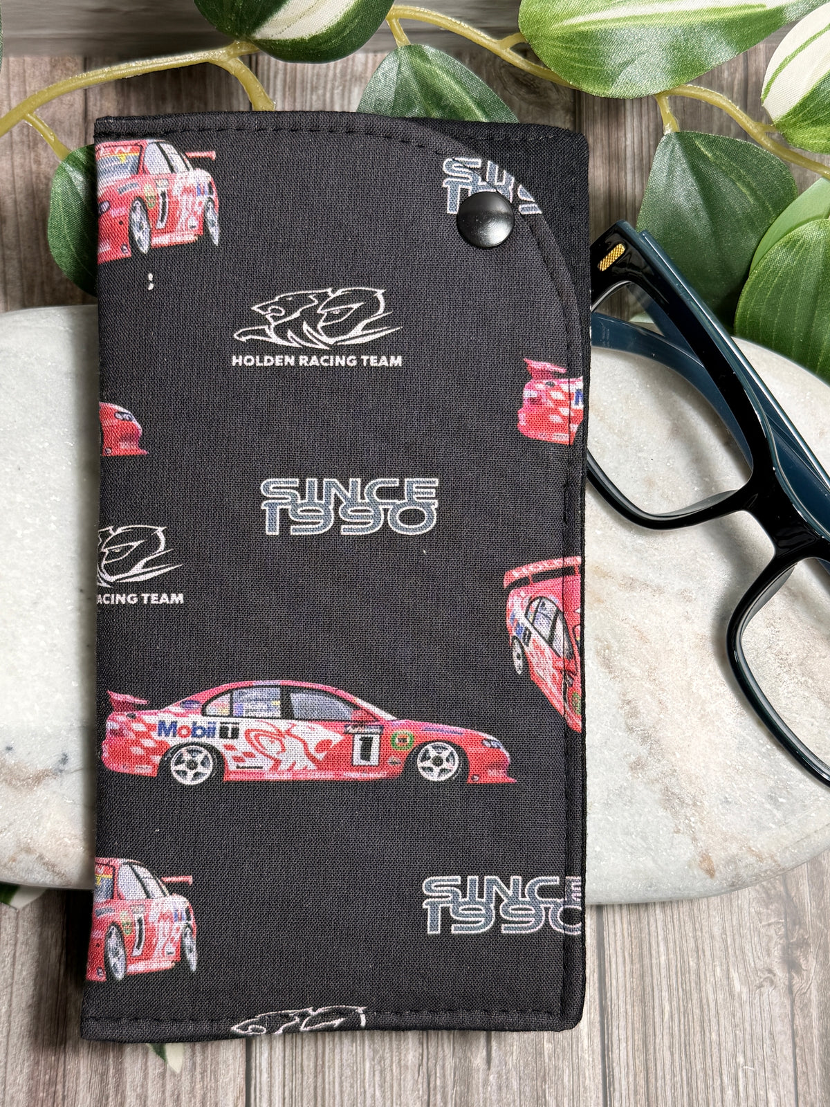 Glasses Case with a Black Holden Racing Team car illustrations on a wooden surface. with glasses