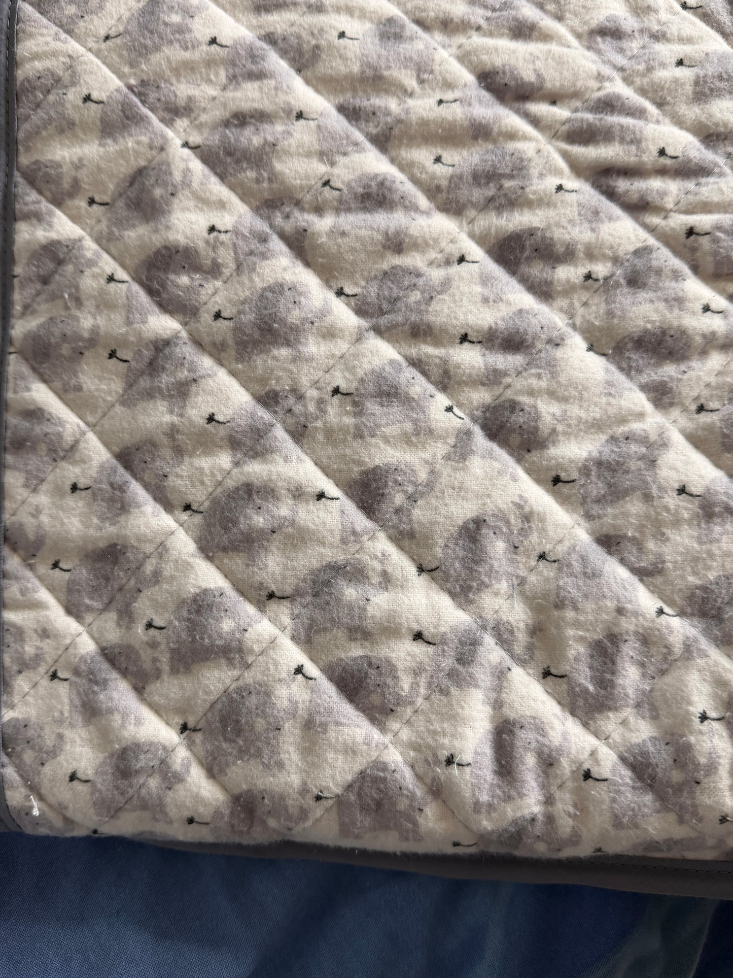 Close-up of a quilted fabric snuggle blanket with a gray and beige elephant pattern, stitched in a diamond pattern.