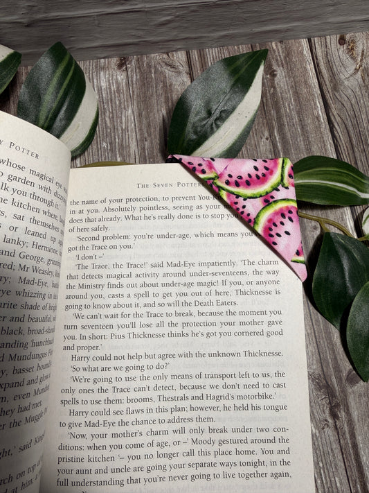 A pink and green watermelon-patterned bookmark is placed on an open book, resting on a rustic wooden surface.