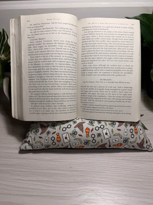 An open book lying on a patterned fabric cushion on a light-colored wooden surface, with a green leaf visible in the background.