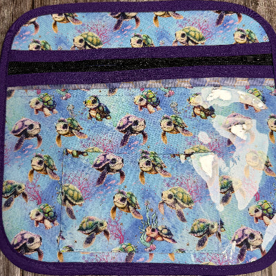 A fabric cross stitch project bag with a purple border and a blue underwater turtle print, featuring a black zipper closure and a clear front pocket.