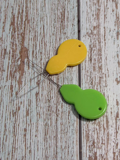 Two colorful long looped needle threader on a wooden surface