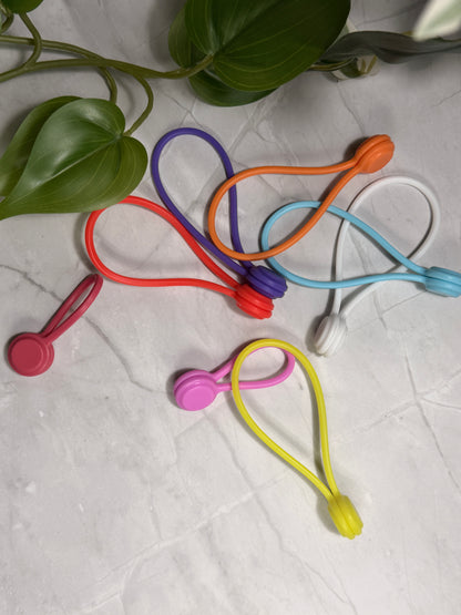 Colorful silicone needle minders on a textured surface with a plant in the corner.