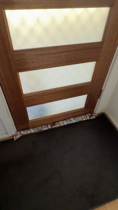 Wooden door with glass panels and a decorative draught stopper with a cat  fabric cover at the base stopping a cold draught.