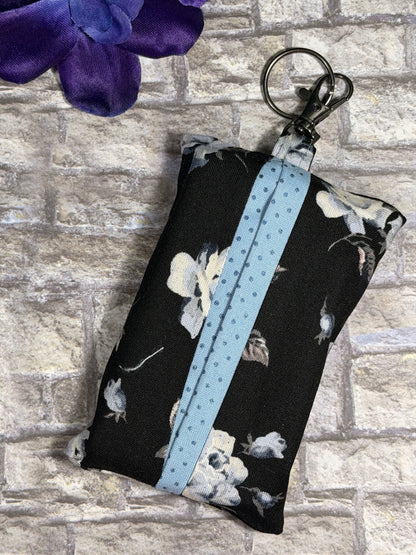 Fabric tissue pouch with a white rose pattern on a keychain against a stone wall background