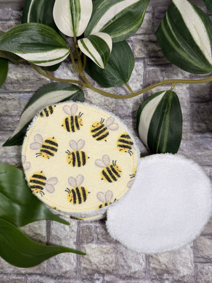 Round fabric face cleanser and make up remover pads with bee pattern on a stone surface with green leaves