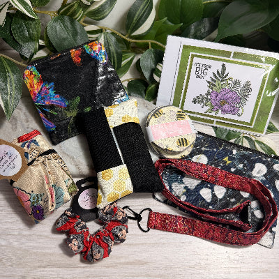 Collection of colorful accessories including a lanyard, cards, and scrunchies on a marble surface with green leaves.