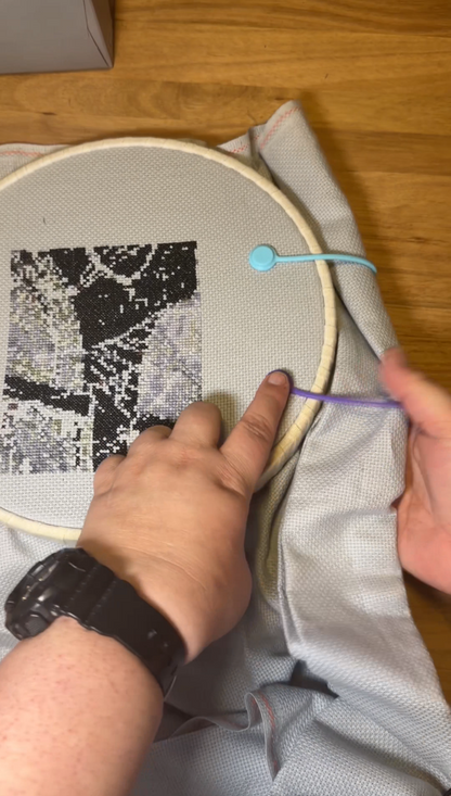 Person working on a cross-stitch project with an embroidery hoop with the silicone needle minder on the project.