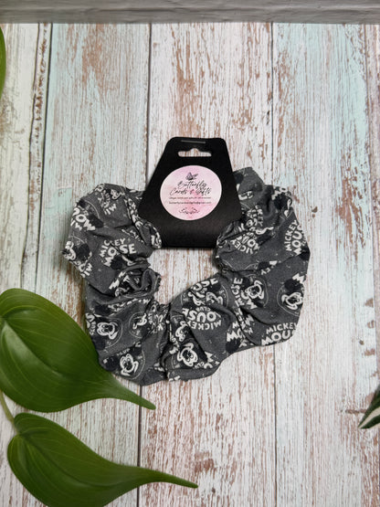 Gray Mickey Mouse patterned scrunchie with a label on a wooden surface