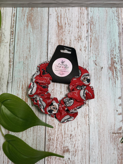 Red scrunchie with black and white design on a wooden surface with a plant leaf.