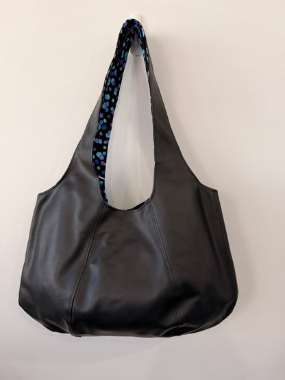 Black leather bag with a blue patterned strap on a light gray background