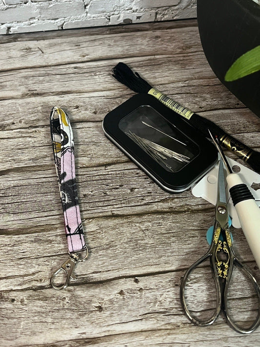 Scissors, lanyard, and black case on a wooden surface with a stone wall background