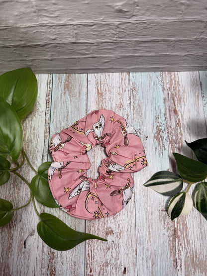 Pink scrunchie with cartoon characters on a wooden surface with green leaves.